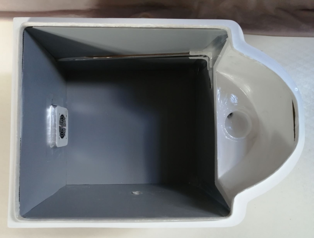 こまらんeトイレは４つのパーツに分かれます。まず、本体ケースで、ケース前部に尿を受ける受け皿、側面に尿を屋外に出す尿配管、後方に排気装置が付いています。